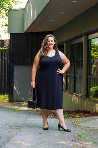 Woman outdoors in a sleeveless black dress with scoop neckline and black heels