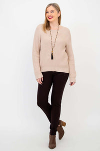 Woman smiling in beige knit sweater, brown pants, and ankle boots