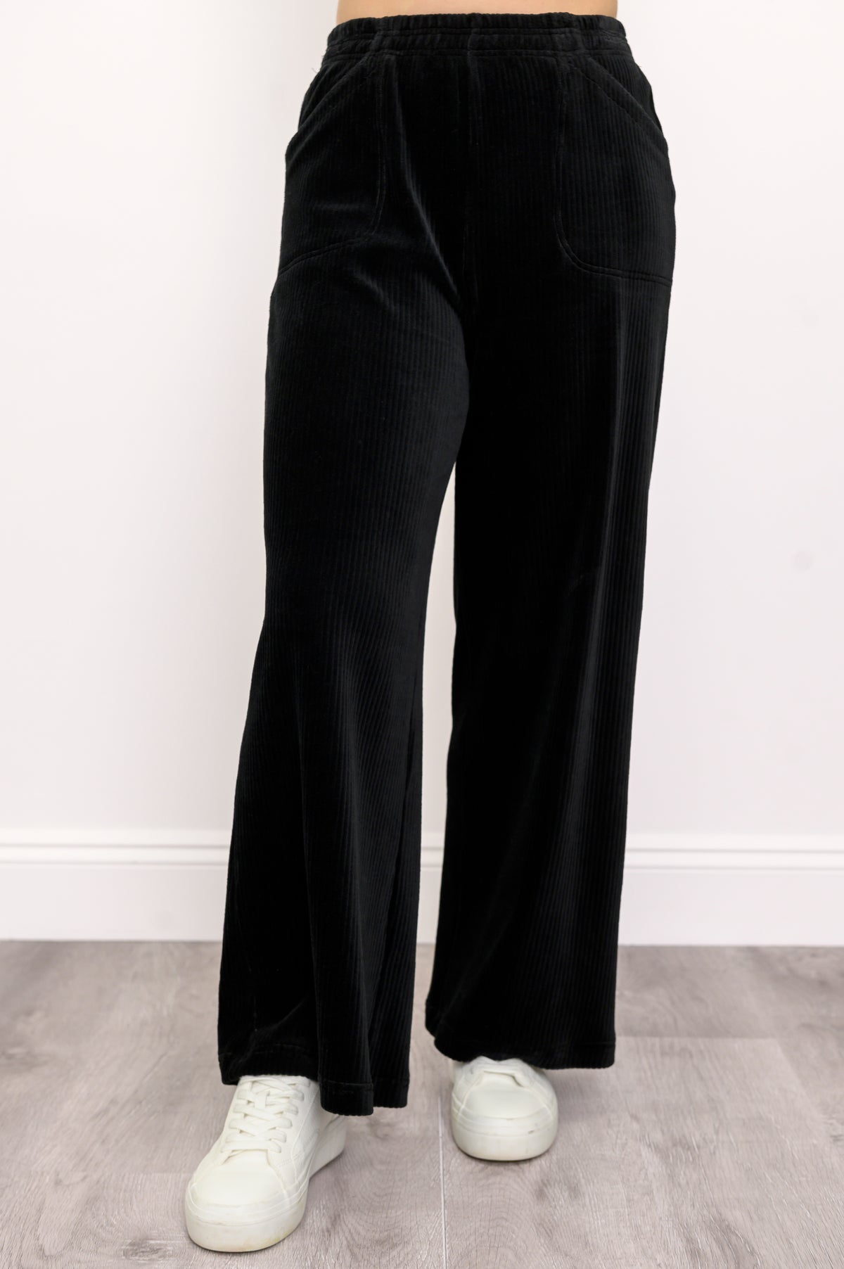 Woman wearing black wide-leg corduroy pants and white shoes on a white background, front view