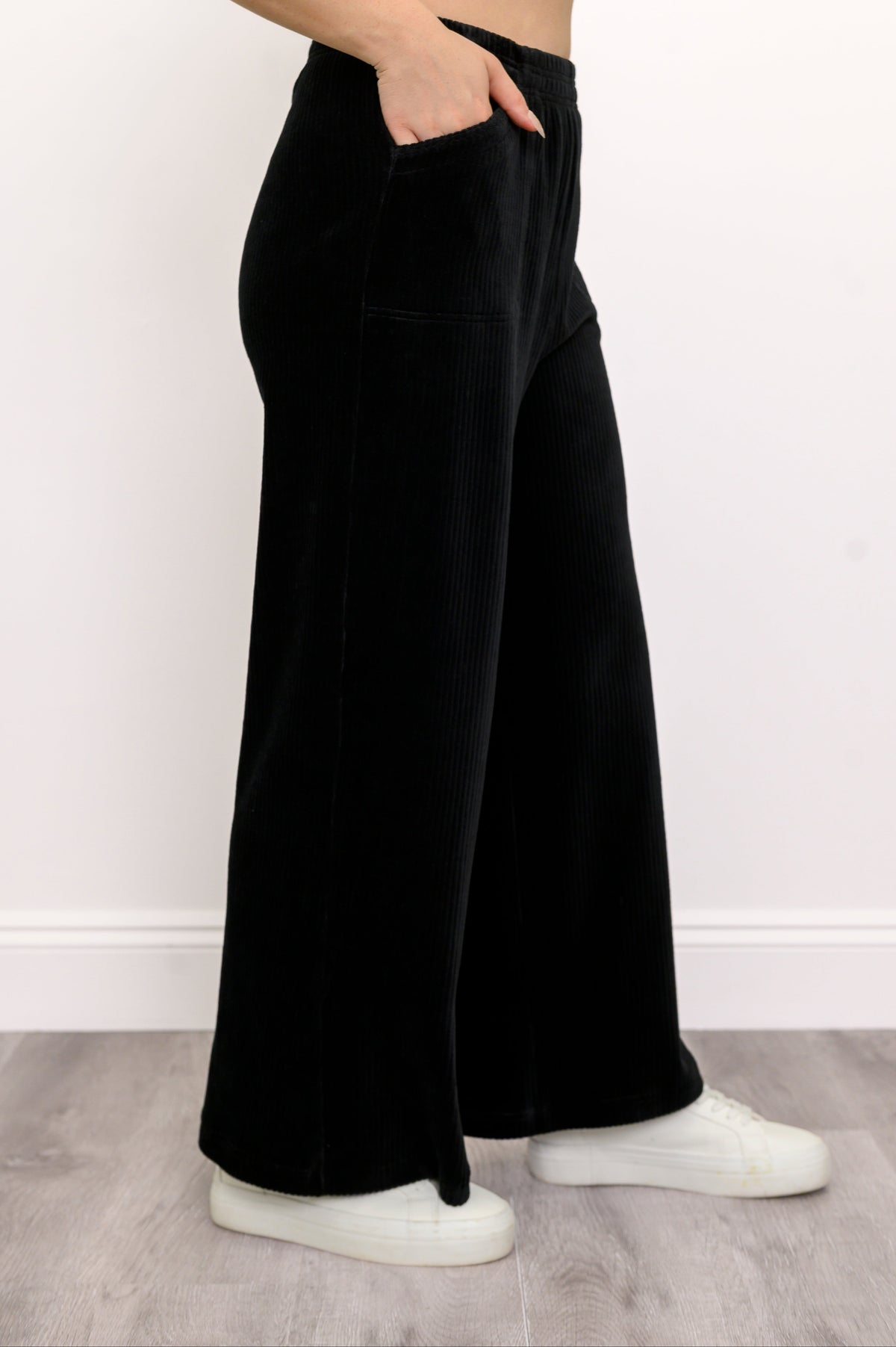 Side view of black wide-leg corduroy trousers with front pockets and an elastic waist