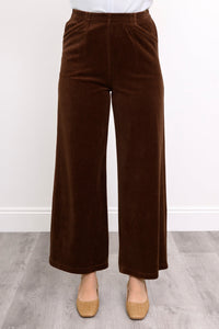 Front view of model wearing brown velvet wide-leg pants worn against white wall on a light gray floor.