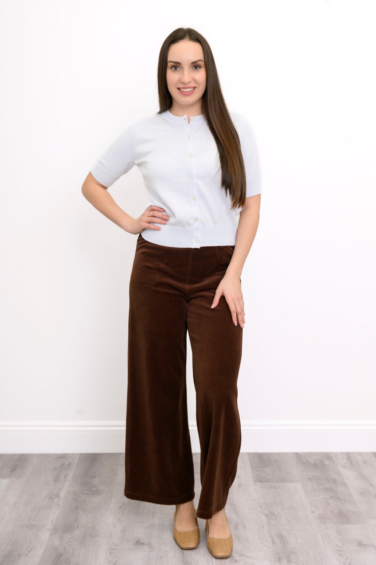 Woman wearing a white knit top, brown cordoroy pants, and tan shoes on a white background