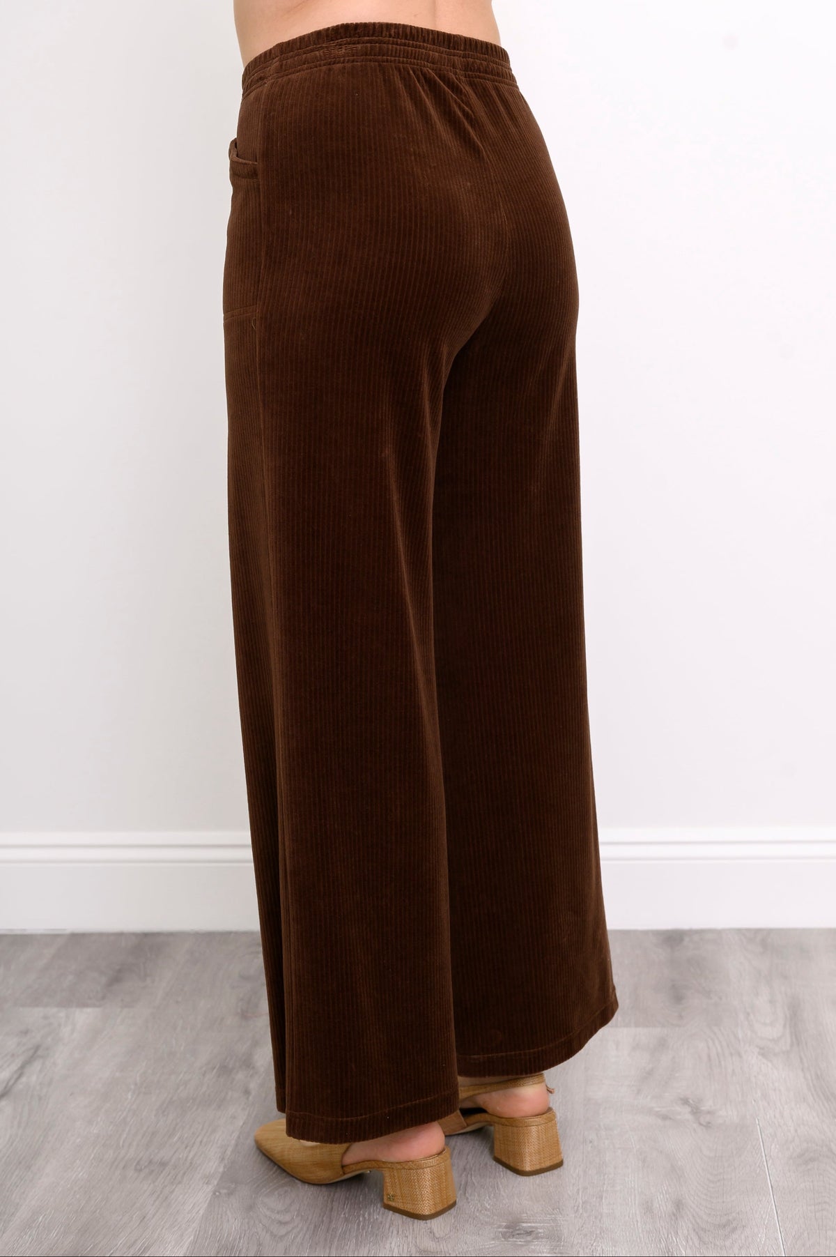 close-up back view of woman wearing highwaisted deep brown corduroy pants  featuring elastic waistband and wide-leg