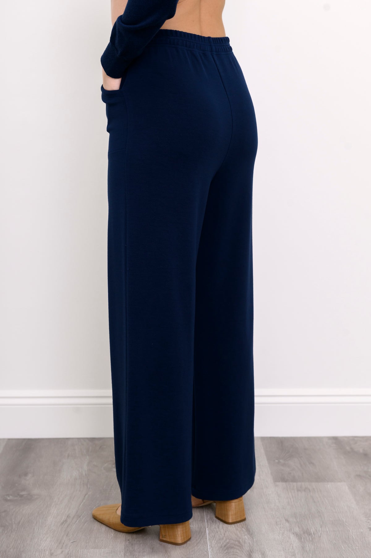 Angled view of woman with her hand in her pocket wearing dark blue pants with beige shoes
