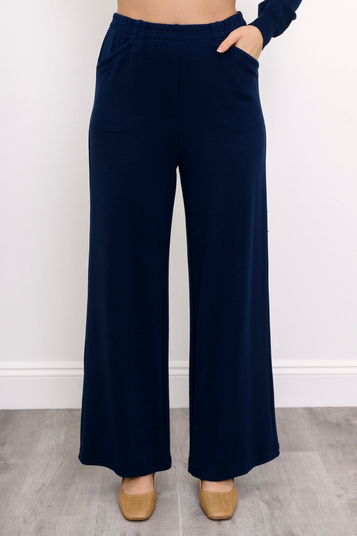 Woman wearing navy blue wide-leg knit pants and tan shoes on a white background, front view
