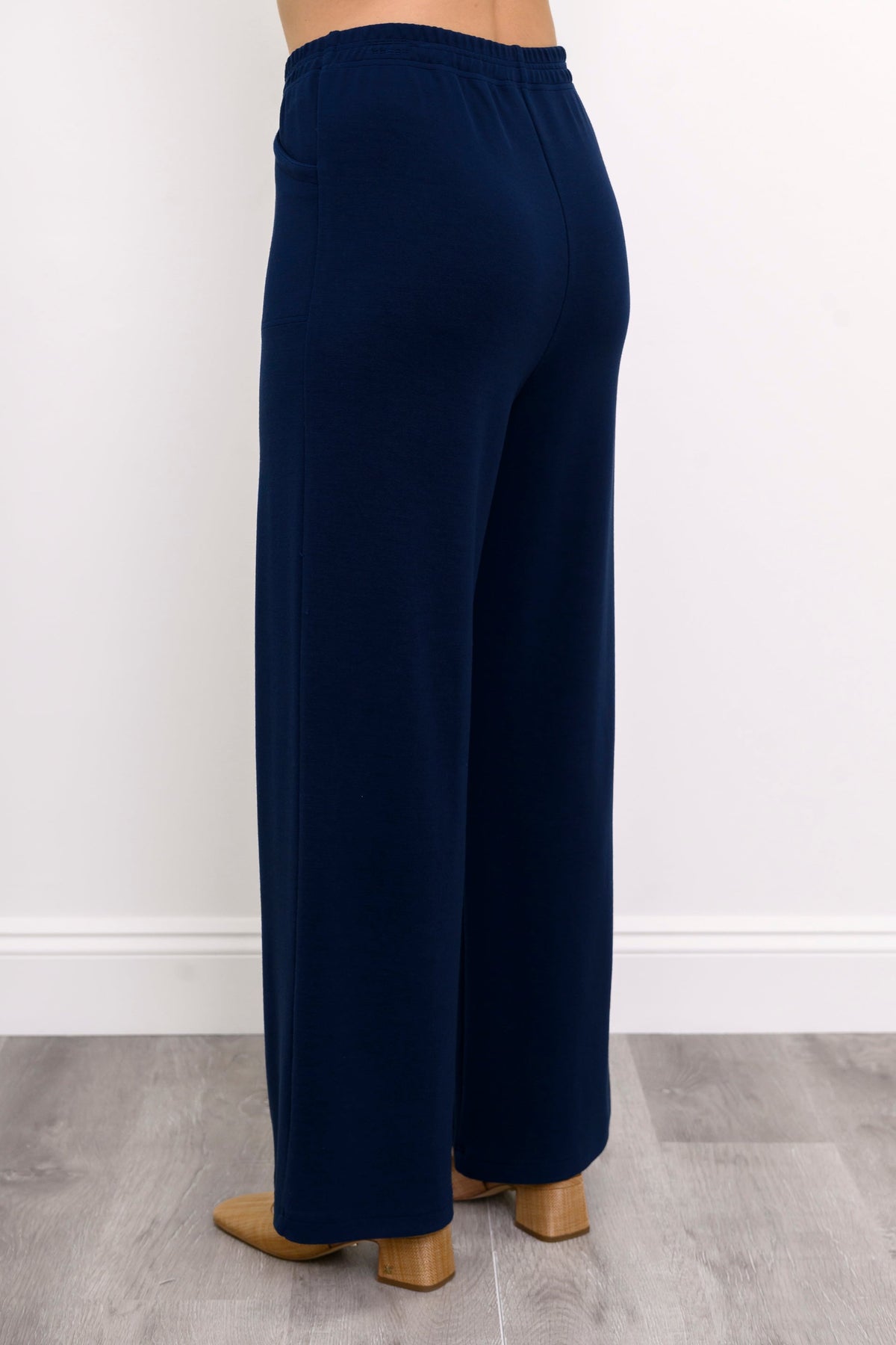 Rear angled view of woman wearing high-waisted navy blue pants with elastic waistband