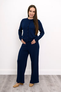Woman modeling a hip length dark navy button down crewneck cardigan with matching blue trousers.