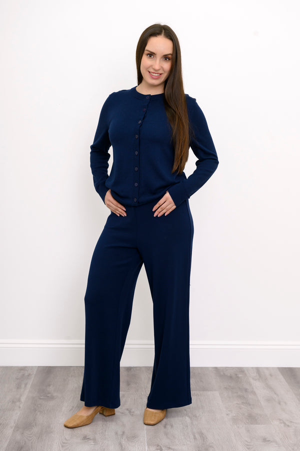 Woman modeling a hip length dark navy button down crewneck cardigan with matching blue trousers.