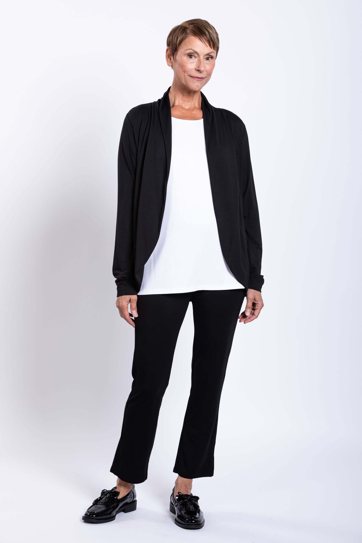 Woman in black French Terry jacket, white top, and black pants, partial side view