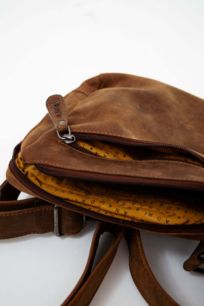 Partially opened brown leather crossbody bag revealing yellow interior