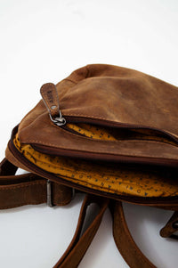Partially opened brown leather crossbody bag revealing yellow interior