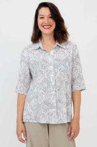 Woman wearing a patterned white and grey button-up blouse with a shirt collar and elbow-length sleeves