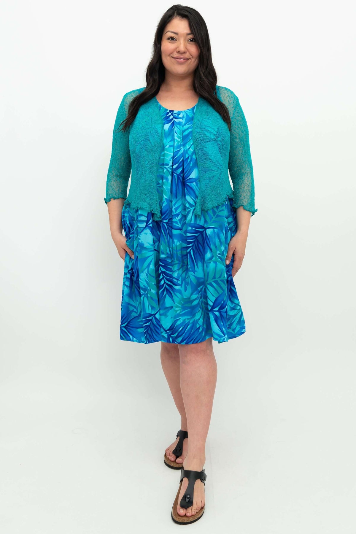 Woman modeling blue leaf print dress with teal cardigan, front view