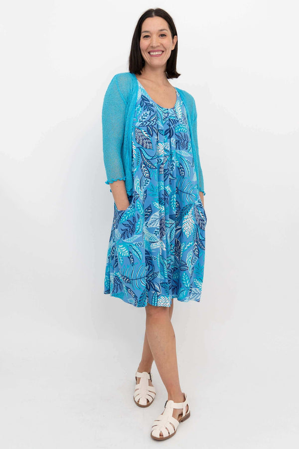 Woman in blue leaf dress layered with a light blue cardigan, standing and smiling