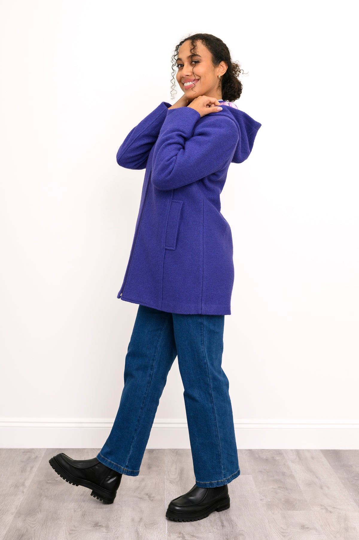 Side view of woman posing in purple/violet hooded jacket with denim pants and back boots