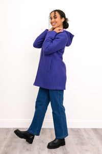 Side view of woman posing in purple/violet hooded jacket with denim pants and back boots