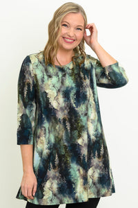 Smiling woman wearing a blue-green watercolor forest print A-line tunic with 3/4 sleeves, front view.