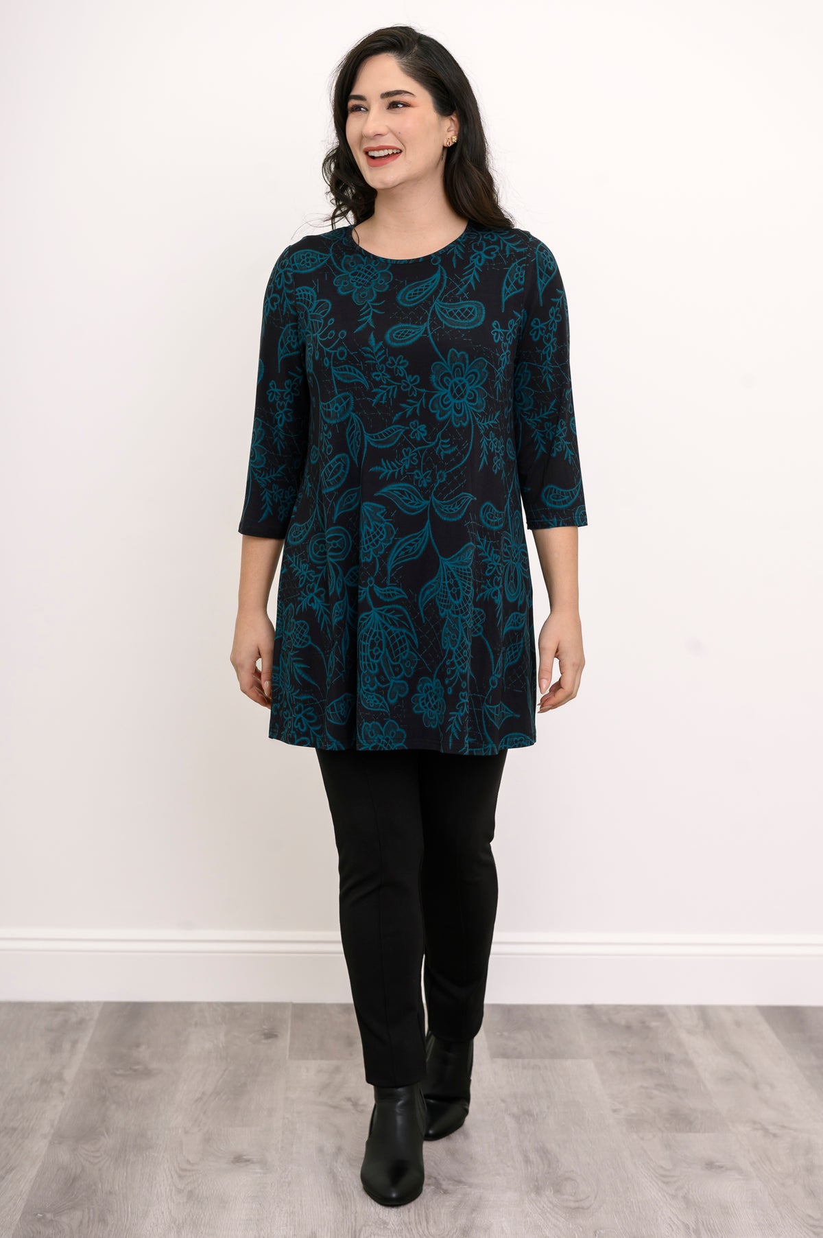 Women's three-quarter sleeve knit tunic in a dark floral print, paired with black trousers in a casual pose.