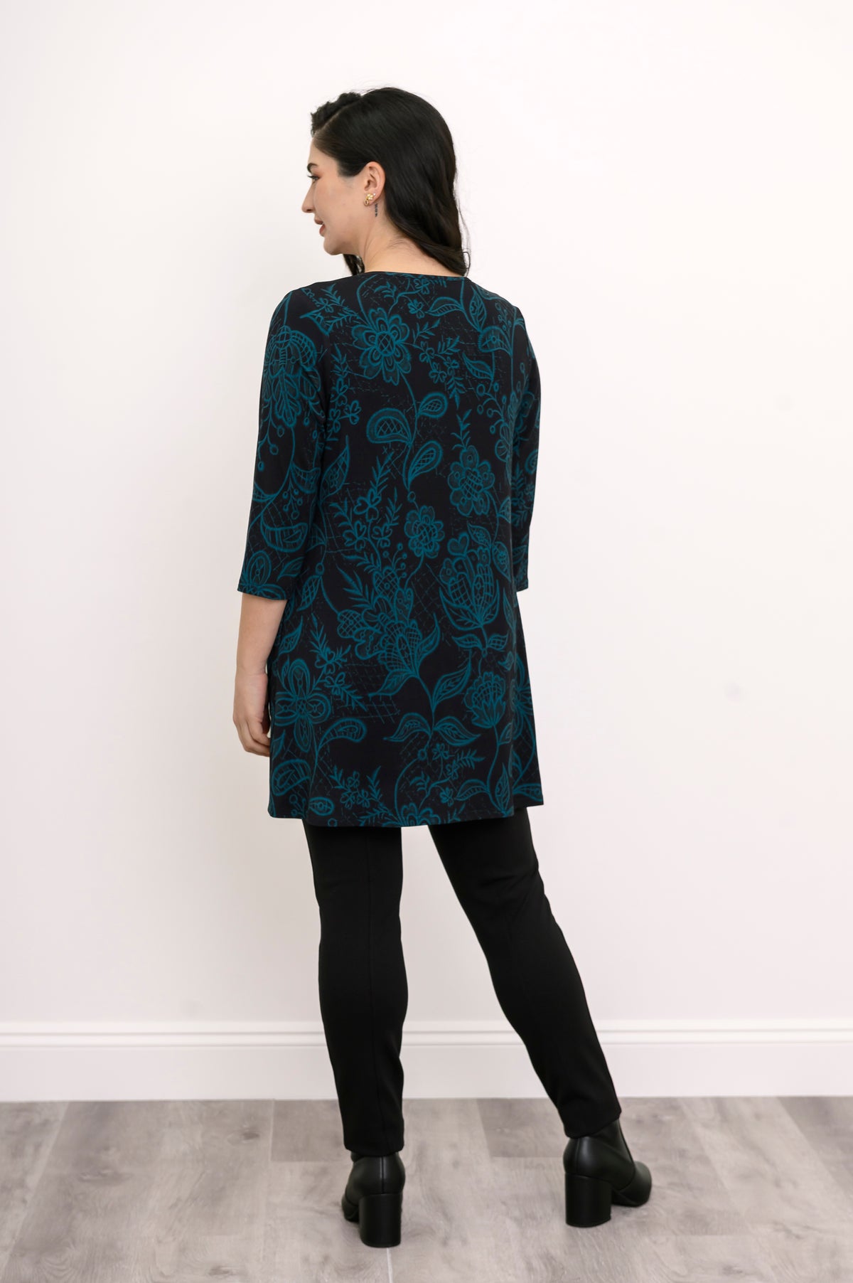 Back view of a women's A-line leaf print bamboo-cotton top, styled with black trousers against a white wall.