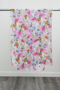 A large silk scarf with a pink and multicolour floral pattern displayed on a metal rod against a white background, front view