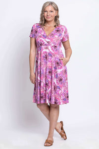 Woman wearing a pink and purple floral bamboo crossover dress, hand in pocket