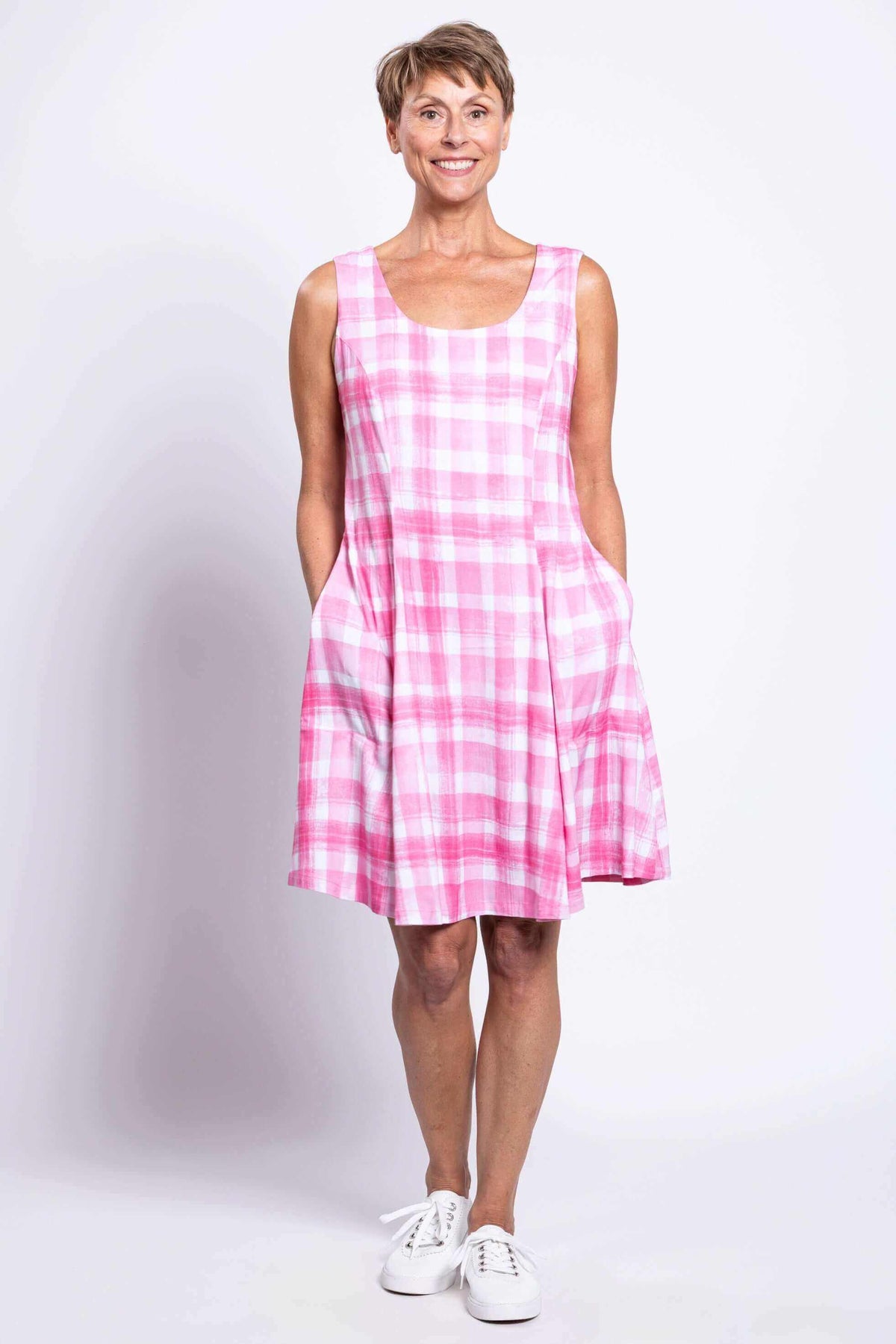 Woman modeling pink plaid summer dress with hands in pockets, front view