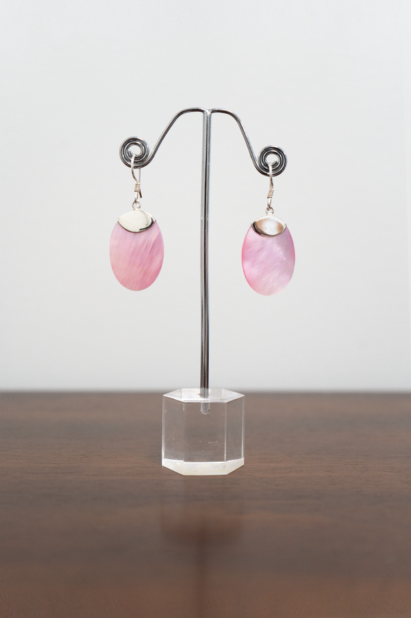 A pair of sterling silver earrings with flat oval shaped pink shell pendants displayed on a metal stand