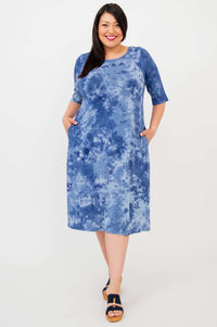 Woman in a plus size blue tie dye dress with pockets, smiling at the camera