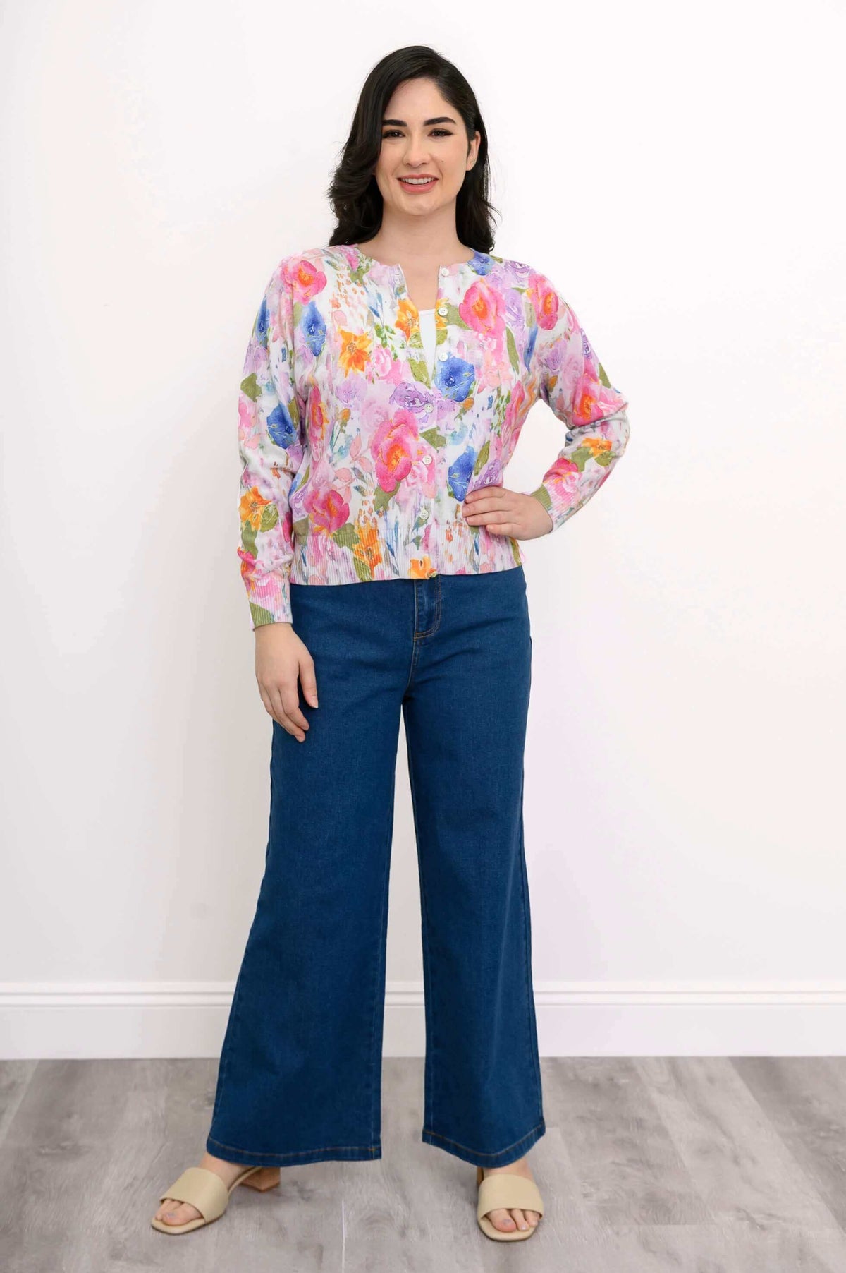 Woman posing with hand on hip in vibrant floral cardigan and high-waisted blue jeans