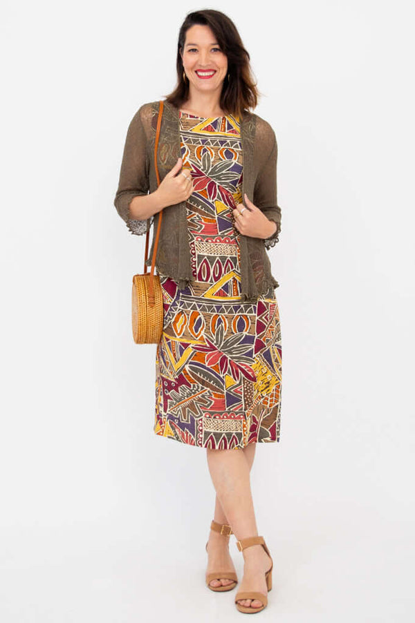 Woman layering printed shift dress with a green cardigan and round bag