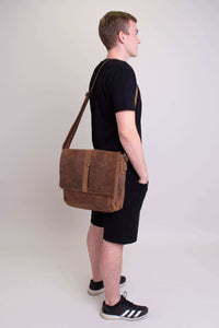 Man standing in profile carrying brown buffalo leather messenger bag over his shoulder
