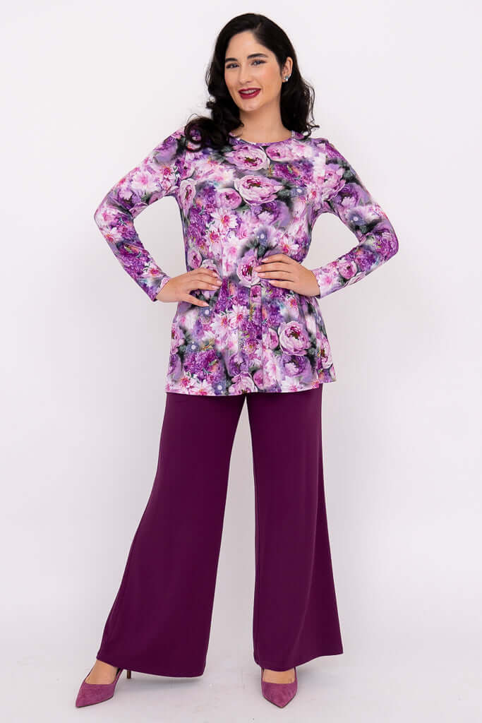 Woman posing in purple floral tunic with hands on hips and purple pants