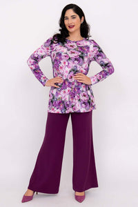 Woman posing in purple floral tunic with hands on hips and purple pants