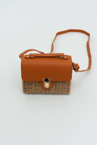 Rattan crossbody bag with brown faux leather flap and gold clasp on white background