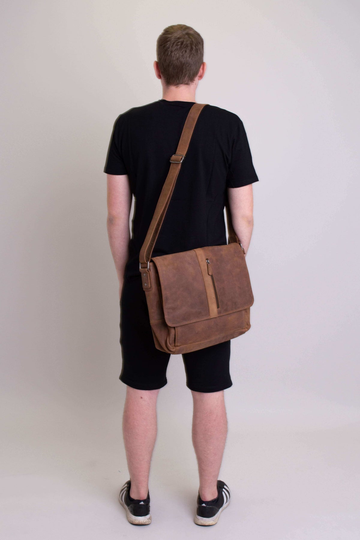 Rear view of man in black outfit with brown buffalo leather messenger bag on his back
