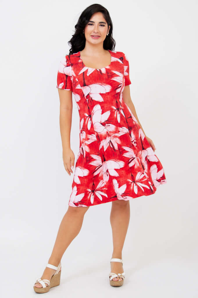 Woman wearing a knee-length red dress with bold white floral print, posing with one knee bent.