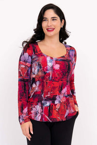 Woman wearing a red floral sweetheart neckline long sleeve top, smiling