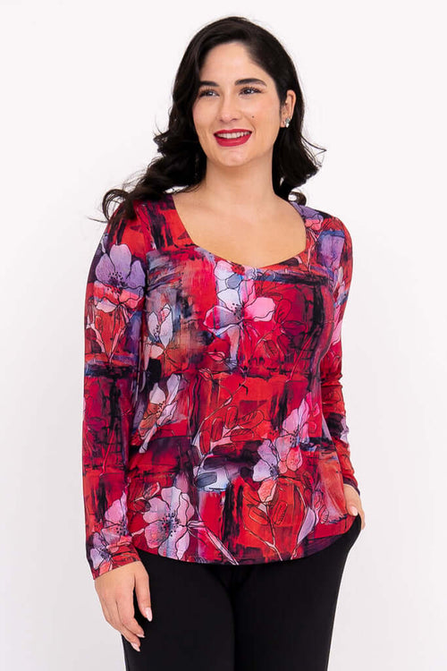 Woman wearing a red floral sweetheart neckline long sleeve top, smiling