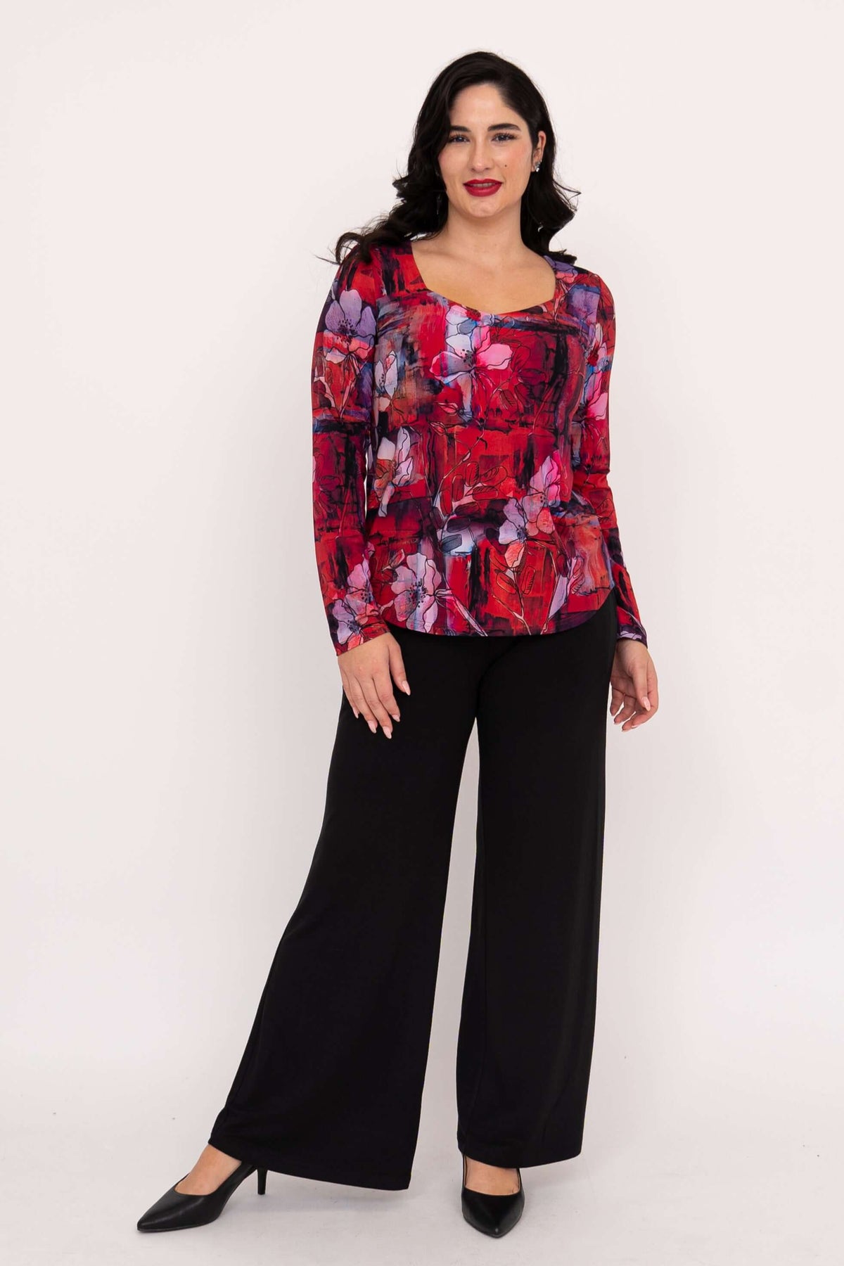 Front view of woman in red floral long sleeve sweetheart top and black pants