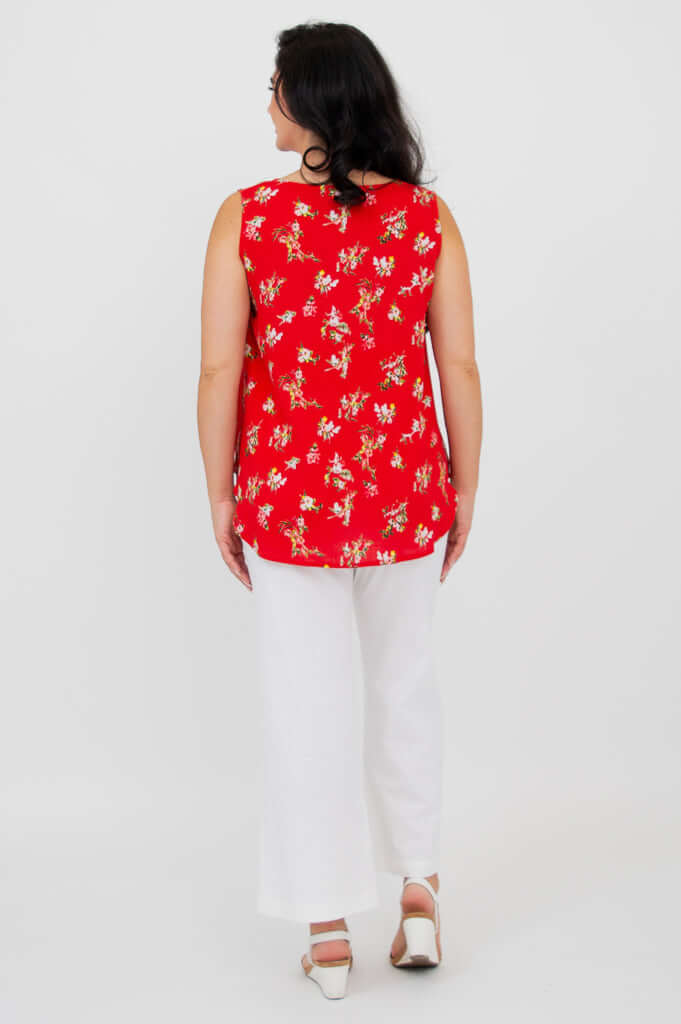 Woman showing back of red floral tank top with white pants