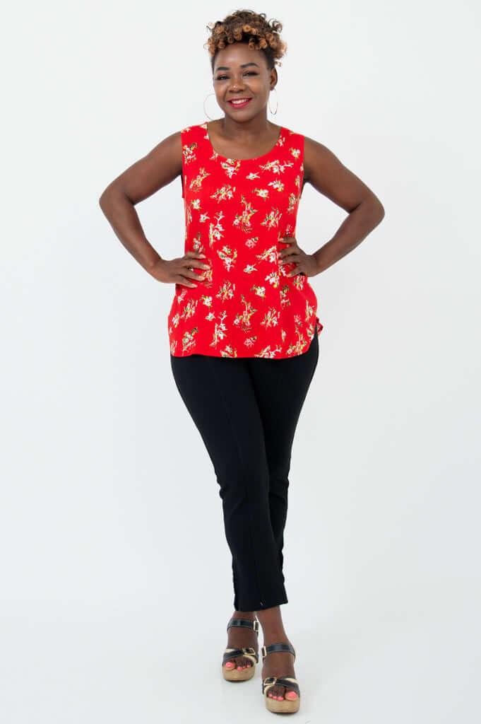 Woman in a red floral tank top and black pants, hands on hips, full body