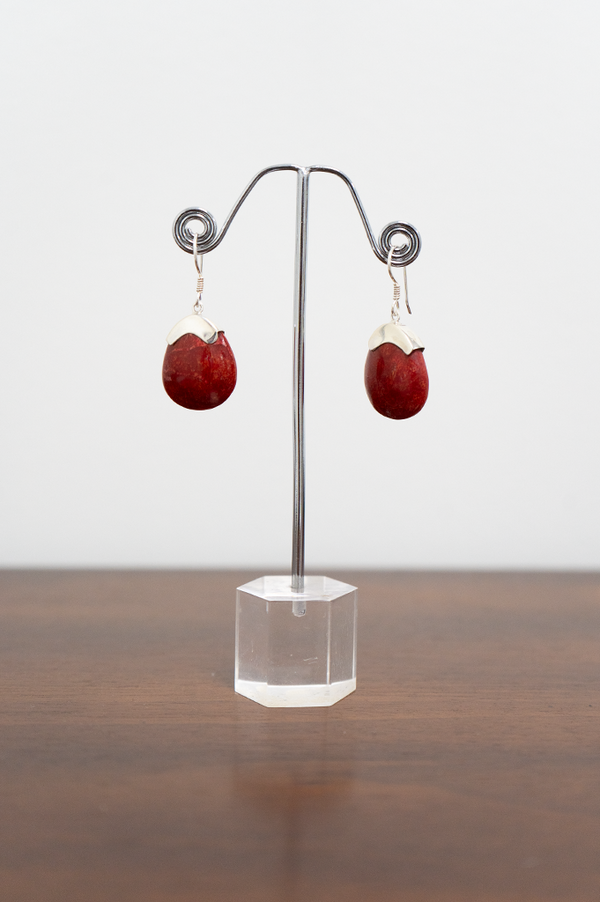 A pair of sterling silver earrings with red stone pendants displayed on a metal stand on a white background, front view
