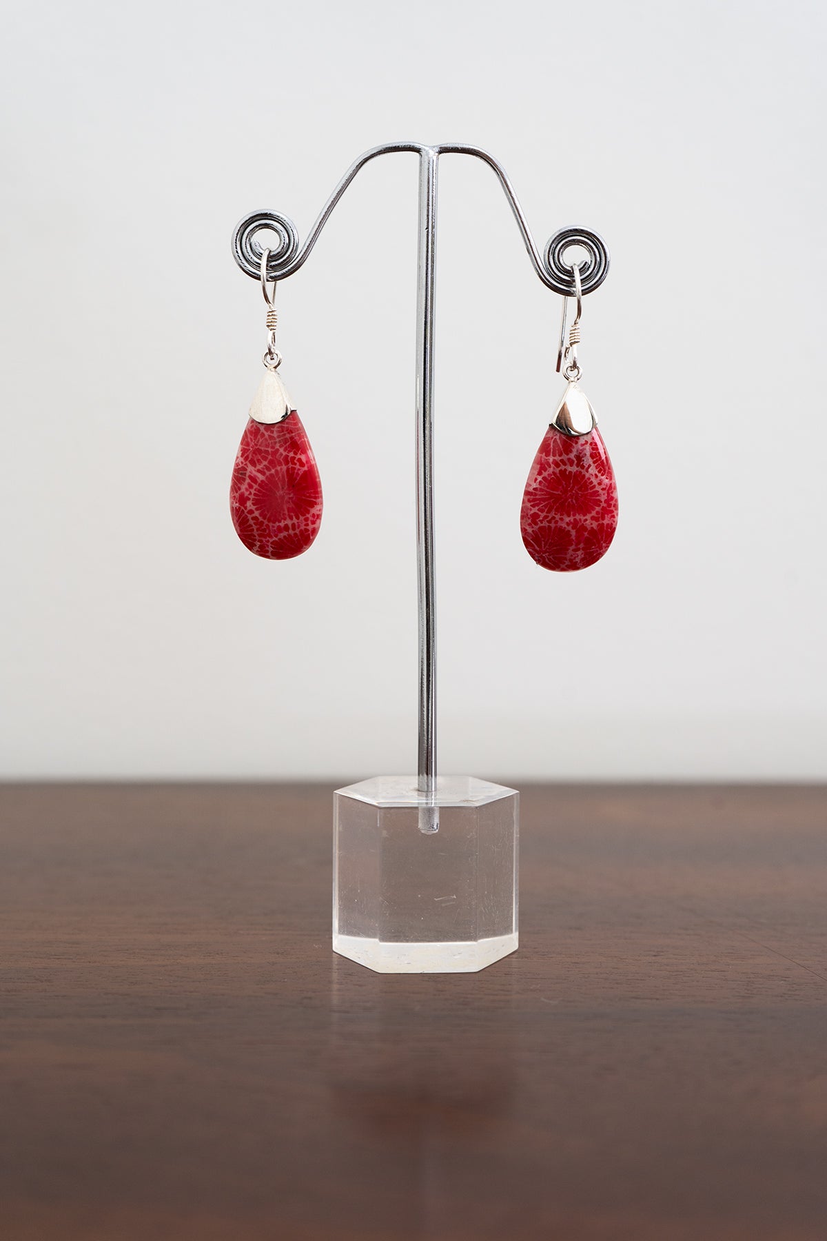 A pair of sterling silver earrings with red marble stones displayed on a metal stand and a white background, front view