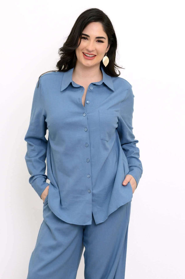 Woman wearing a relaxed blue button-up shirt and matching pants, hands in pockets