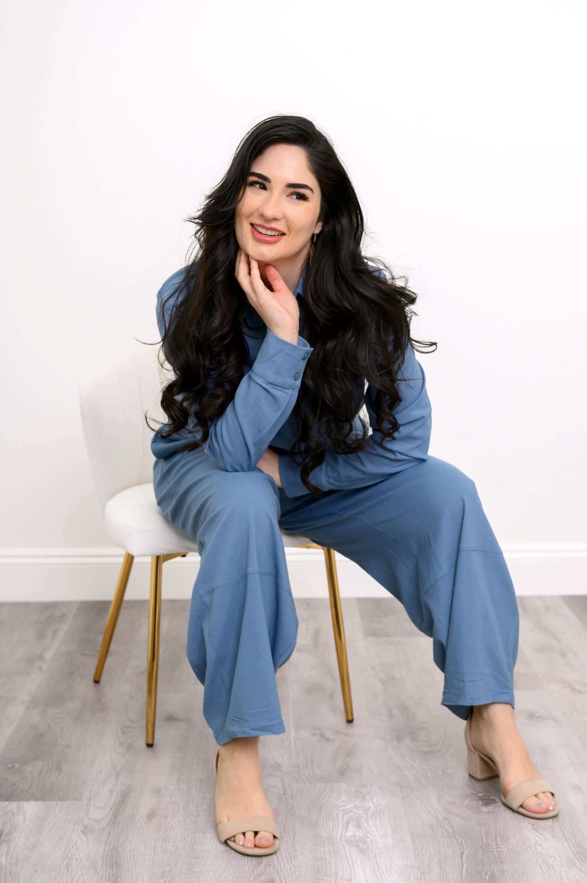 Seated woman in relaxed blue shirt and pants, smiling with hand on chin