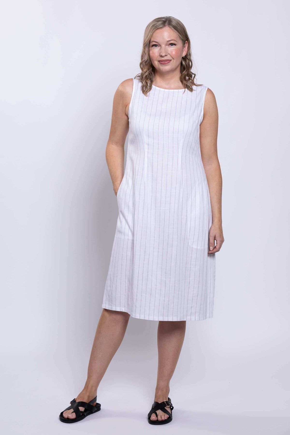 Front view of woman standing in white sleeveless striped dress with relaxed pose