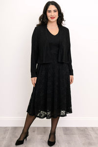 Front view of female model wearing a black lace dress with a matching jacket against a white background with gray floor