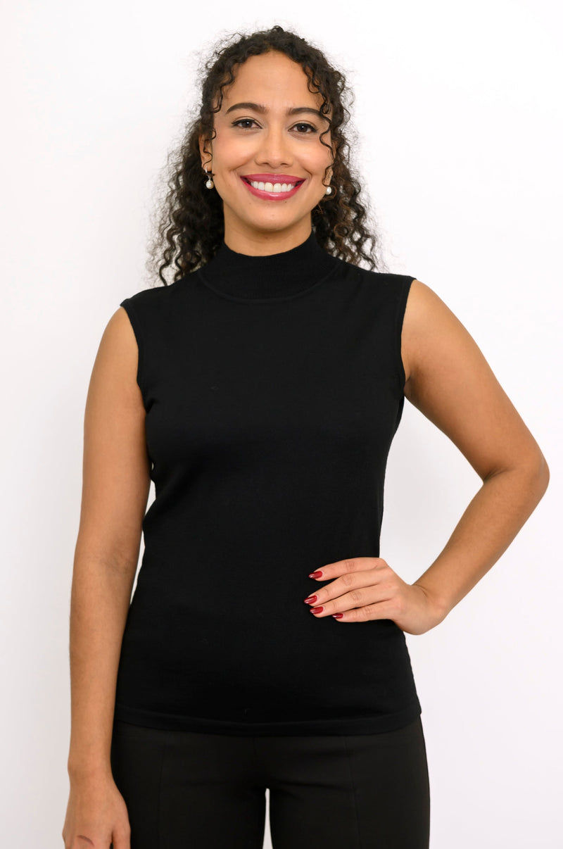 A smiling woman with curly hair wearing a black sleeveless mock neck top and black pants, posing against a plain white background.