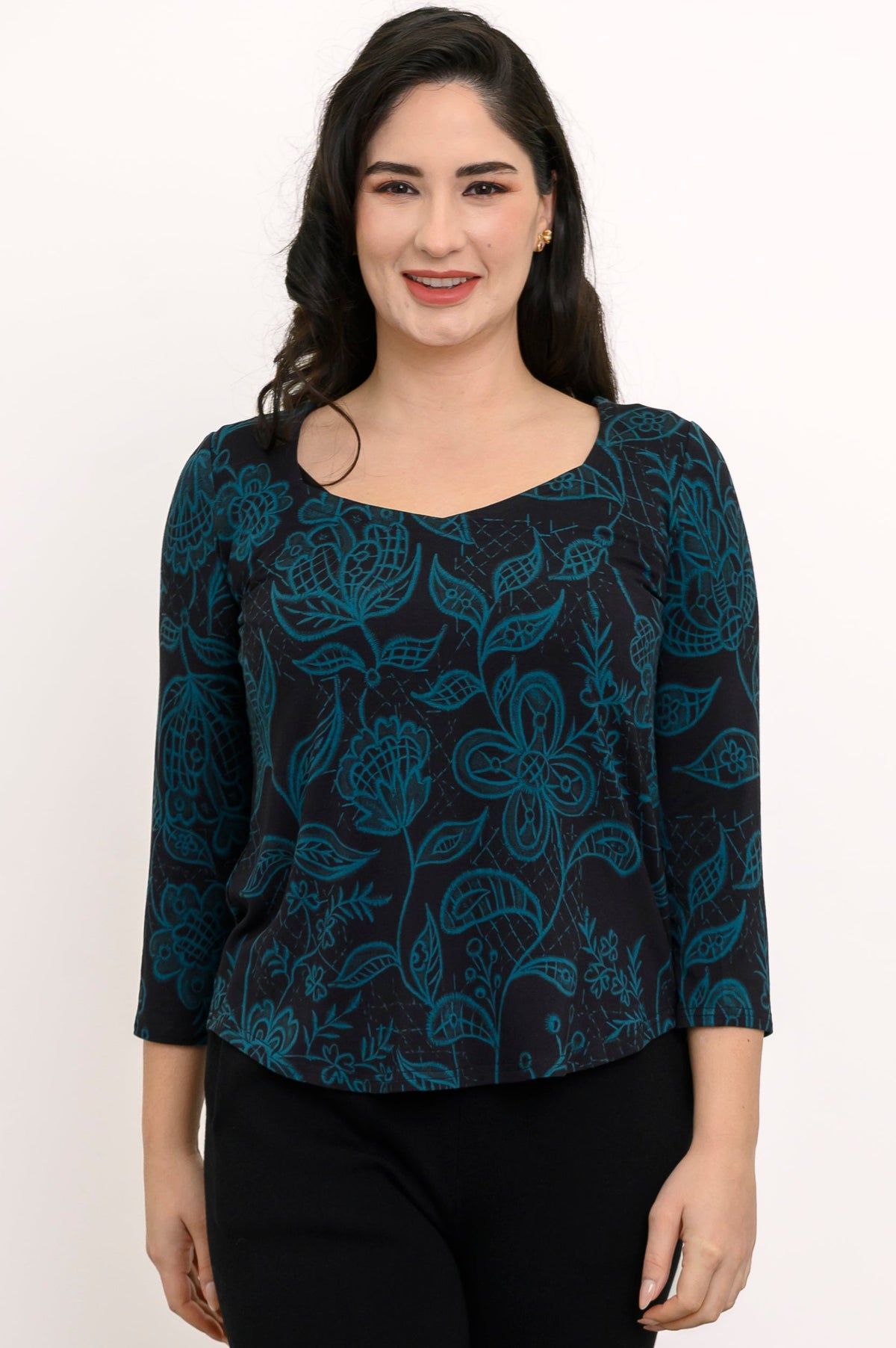 Smiling woman wearing a black knit top adorned with a teal foliage pattern, featuring a sweetheart neckline.