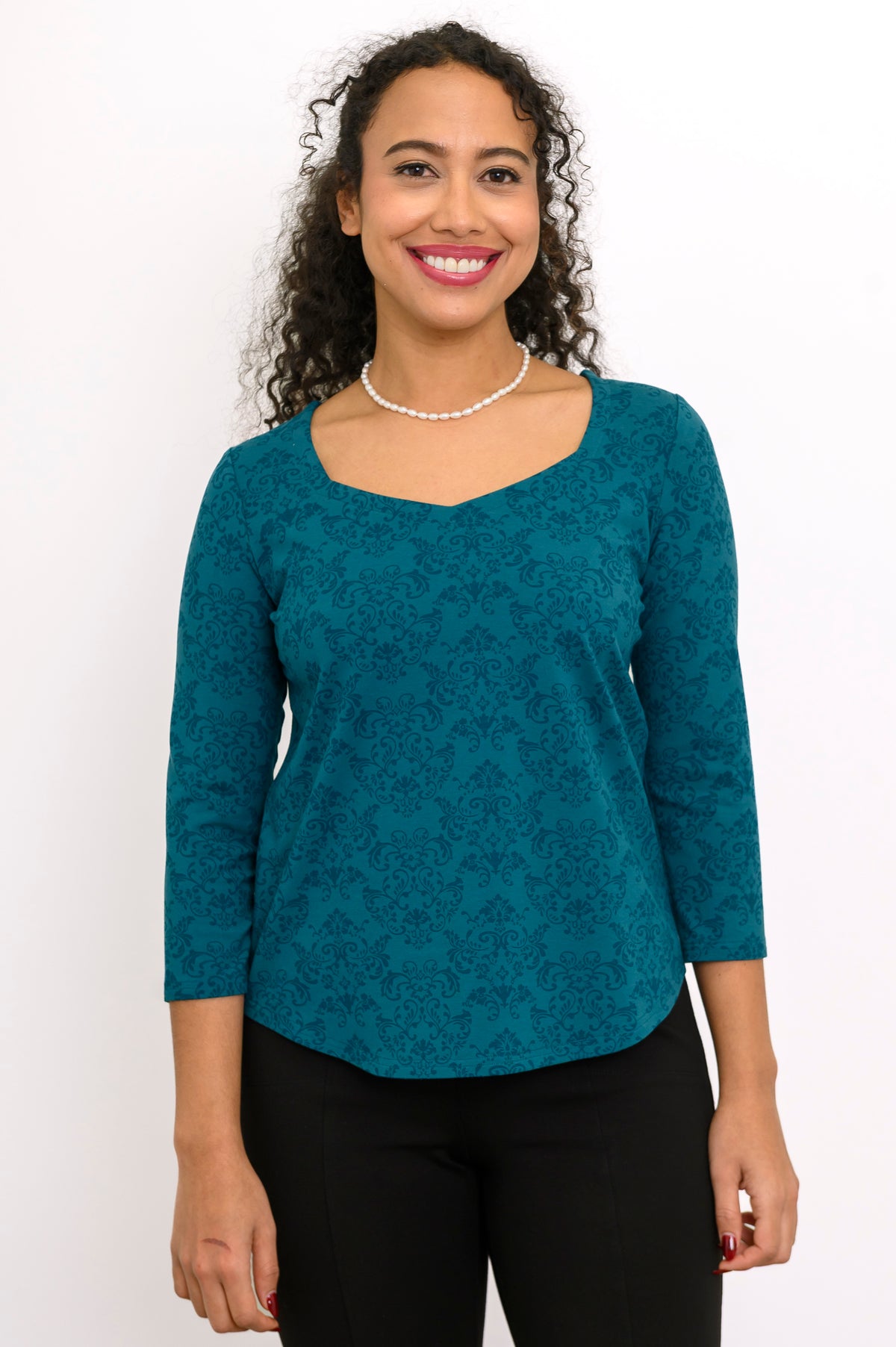 Smiling woman wearing a teal geometric print bamboo-cotton top with a sweetheart neckline and 3/4 sleeves, front view.